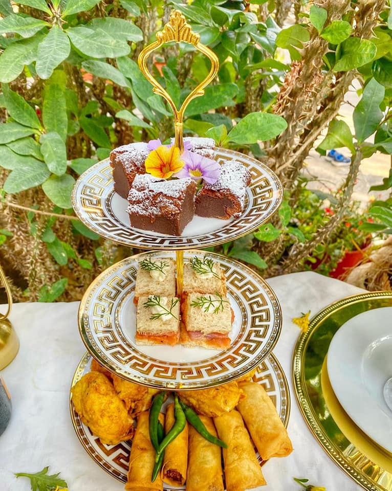 Three-tier gold-rimmed afternoon-tea tower with brownies, finger sandwiches, satay and spring rolls in a garden