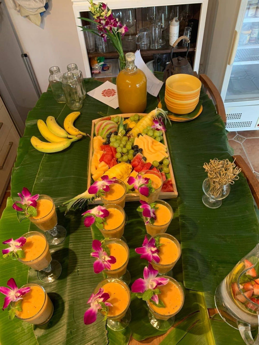 Banana-leaf dessert table with orchid-topped sweet treats and fresh fruit