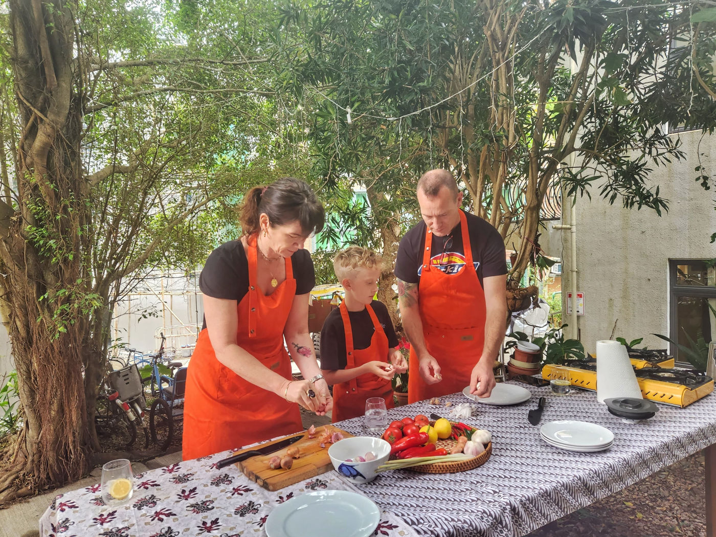Family cooking class in Lantau — students in orange aprons prepping lemongrass, chilies and aromatics outdoors