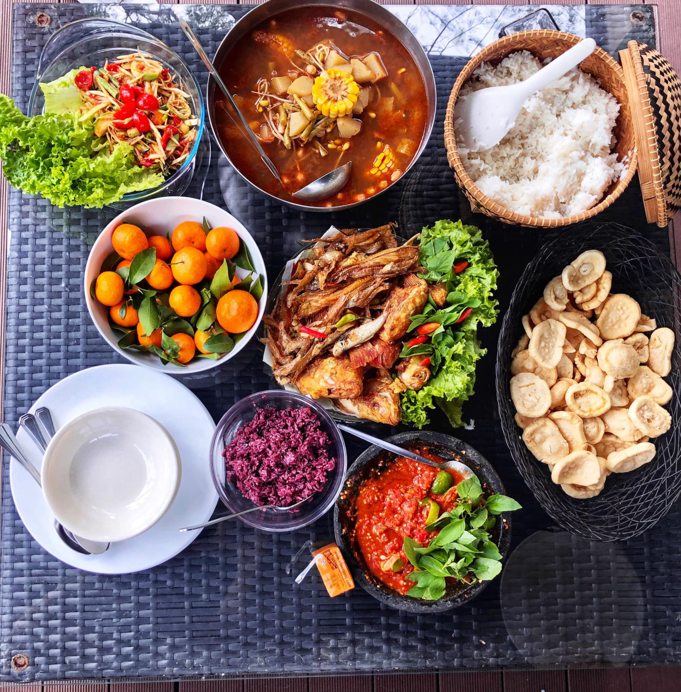 Indonesian feast spread with slow-braised curries, sambal in a stone cobek, fried fish, black rice and crackers