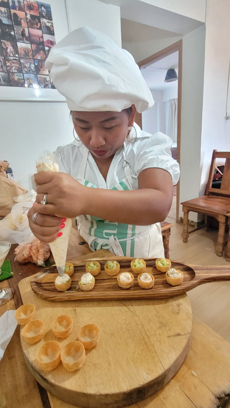 Chef Novy in a white chef's hat and apron, carefully piping freshly made canapés onto a wooden serving board
