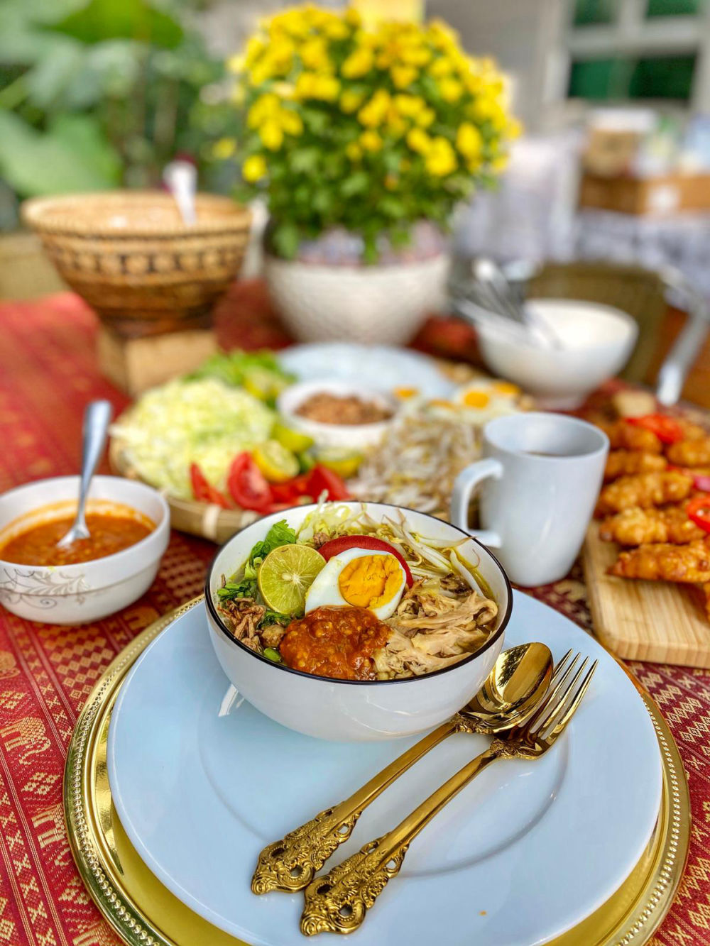 Indonesian soto soup with egg and lime served with ornate gold cutlery on a batik table setting