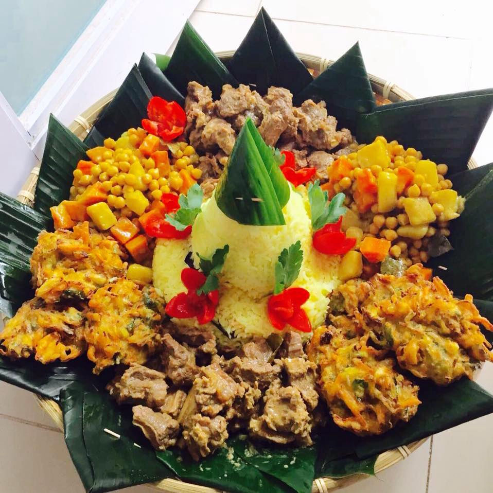 Traditional Tumpeng — yellow nasi kuning rice cone surrounded by rendang, curries and fritters in a woven banana-leaf basket